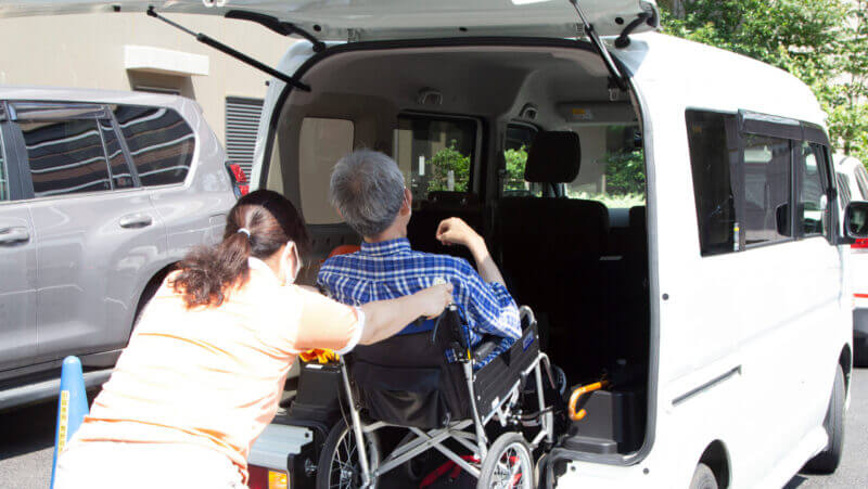 女性介護スタッフの支援で車椅子のまま福祉車両に乗り込む男性高齢者